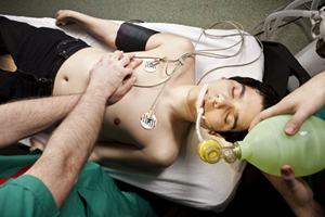 Image of young man having chest compressions done with a manual resuscitator over his mouth